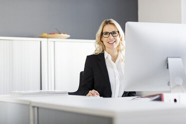 Smiling blond woman at desk in office - PESF000044