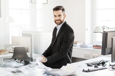 Smiling businessman sitting on desk in office - PESF000122