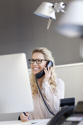 Smiling blond woman in office on the phone - PESF000071