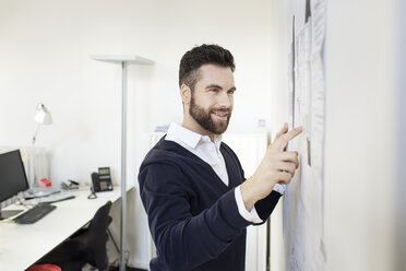Mann in Büro zeigt auf Wand mit Papieren - PESF000080