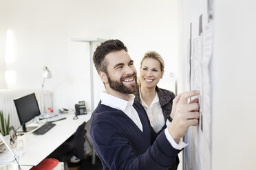 Zwei selbstbewusste Kollegen im Büro an der Wand mit Papieren - PESF000081