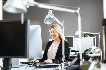 Lächelnde blonde Frau arbeitet am Schreibtisch im Büro - PESF000105