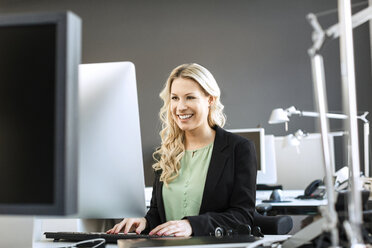 Lächelnde blonde Frau arbeitet am Schreibtisch im Büro - PESF000107