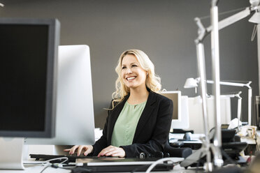 Lächelnde blonde Frau arbeitet am Schreibtisch im Büro - PESF000108