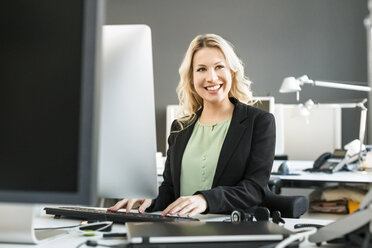 Lächelnde blonde Frau arbeitet am Schreibtisch im Büro - PESF000109