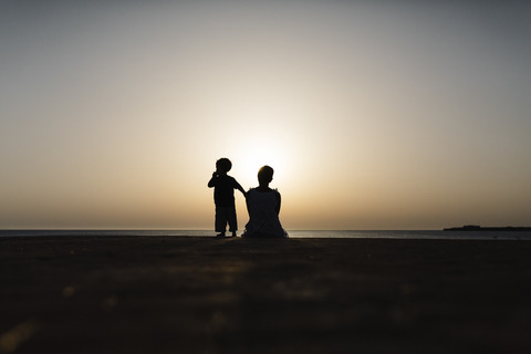 Spanien, Menorca, Silhouette von Mutter und Sohn beim Betrachten des Sonnenuntergangs am Meer, lizenzfreies Stockfoto