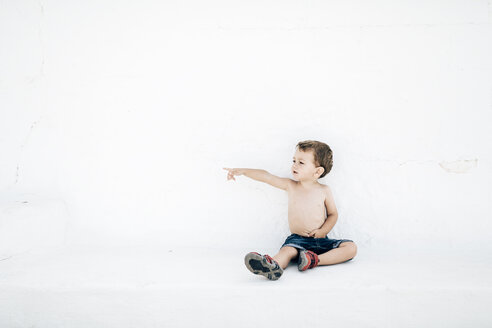 Spanien, Menorca, kleiner Junge ohne Hemd, der vor einer weißen Wand sitzt und auf etwas in der Ferne zeigt - JRFF000010