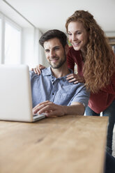 Smiling couple at home looking at laptop - RBF003505