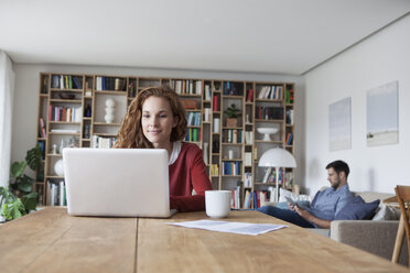 Frau zu Hause mit Laptop und Mann im Hintergrund - RBF003507