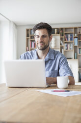 Smiling man at home using laptop - RBF003510