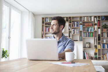 Mann zu Hause schaut vom Laptop weg - RBF003511