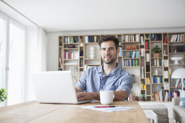 Porträt eines lächelnden Mannes zu Hause am Laptop - RBF003557