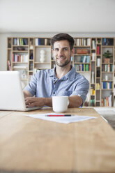 Portrait of smiling man at home using laptop - RBF003558