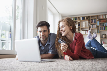 Happy couple lying on floor shopping online - RBF003519