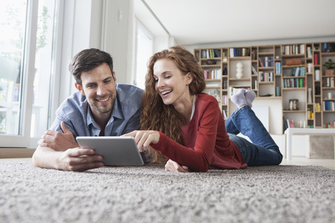 Glückliches Paar auf dem Boden liegend mit digitalem Tablet, lizenzfreies Stockfoto