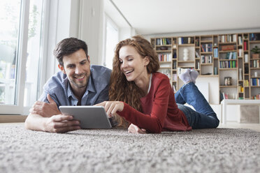 Happy couple lying on floor using digital tablet - RBF003521