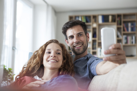 Entspanntes Paar zu Hause auf der Couch, das auf sein Handy schaut, lizenzfreies Stockfoto