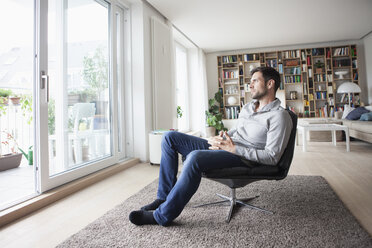 Man at home sitting in armchair looking out of window - RBF003560