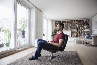 Mann zu Hause im Sessel sitzend und aus dem Fenster schauend - RBF003561