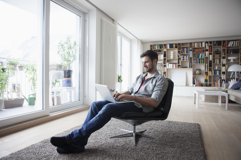 Mann zu Hause im Sessel sitzend mit Laptop, lizenzfreies Stockfoto