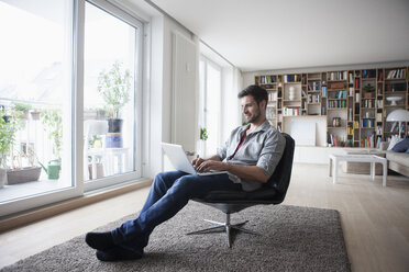 Mann zu Hause im Sessel sitzend mit Laptop - RBF003562