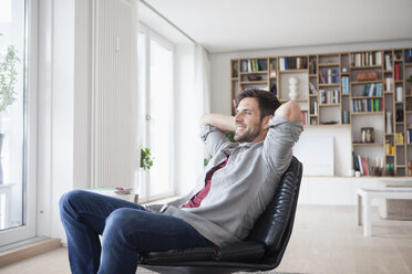 Smiling man at home sitting in armchair with hands behind head - RBF003563