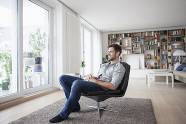 Lächelnder Mann zu Hause im Sessel sitzend und aus dem Fenster schauend - RBF003564