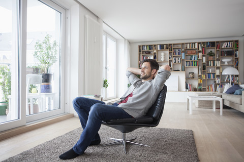 Lächelnder Mann zu Hause im Sessel sitzend mit den Händen hinter dem Kopf, lizenzfreies Stockfoto