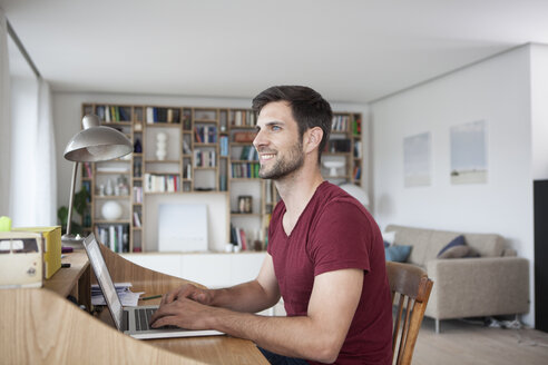 Lächelnder Mann zu Hause am Laptop - RBF003549