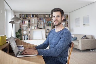 Porträt eines lächelnden Mannes zu Hause am Laptop - RBF003552