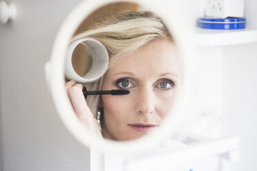 Mirror image of blond woman with curler applying mascara - CHPF000161