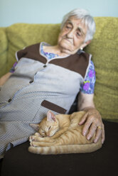 Tabby kitten snoozing besides old woman on the couch at home - RAEF000377