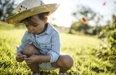 Little girl wearing straw hat crouching on a meadow - MGOF000519