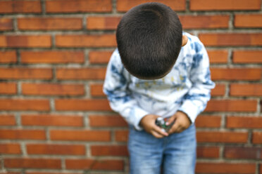 Kopf eines kleinen Jungen, der sich an eine Backsteinmauer lehnt und nach unten schaut - MGOF000529