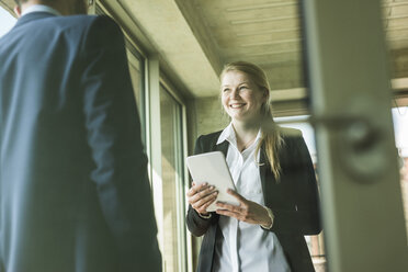 Smiling young businesswoman with digital tablet looking at businessman - UUF005419