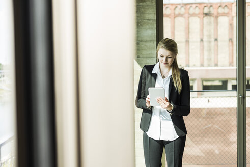 Young businesswoman at the window looking on digital tablet - UUF005420