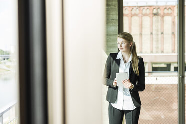 Young businesswoman at the window with digital tablet - UUF005421