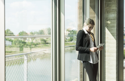 Young businesswoman at the window looking on digital tablet - UUF005422