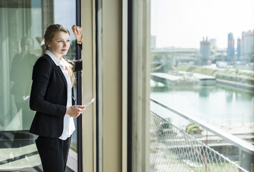 Young businesswoman with digital tablet looking out of window - UUF005423