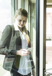 Smiling young businesswoman at the window looking on cell phone - UUF005426