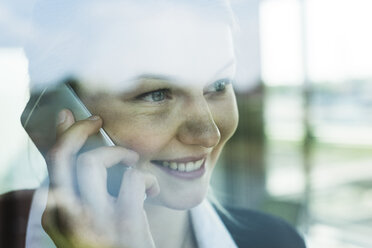 Smiling young businesswoman behind windowpane on cell phone - UUF005429