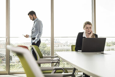 Businessman and young businesswoman in conference room with laptop - UUF005435