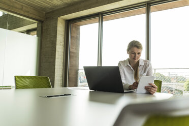 Young businesswoman in conference room with laptop and digital tablet - UUF005443