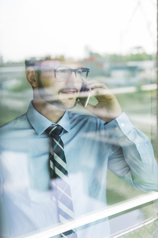 Junger Geschäftsmann am Mobiltelefon hinter einer Fensterscheibe, lizenzfreies Stockfoto