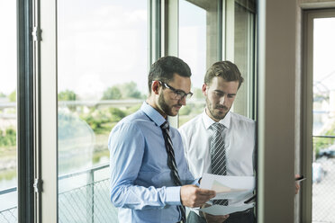 Two young businessmen looking at documents at the window - UUF005456