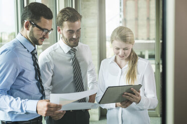 Three young businesspeople looking at documents and digital tablet - UUF005457