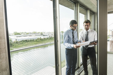 Two young businessmen discussing documents at the window - UUF005462