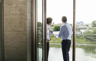 Zwei junge Geschäftsleute stehen auf einem Balkon und diskutieren - UUF005464