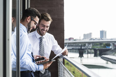 Zwei junge Geschäftsleute mit Dokumenten, Smartphone und digitalem Tablet auf dem Balkon - UUF005467