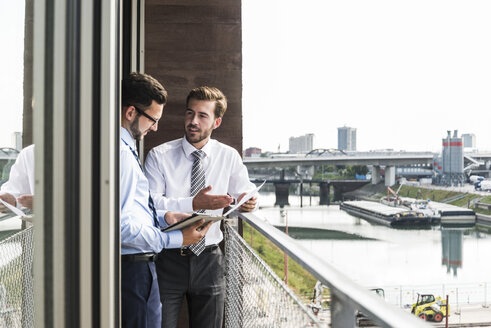 Zwei junge Geschäftsleute mit Dokumenten und digitalem Tablet diskutieren auf dem Balkon - UUF005468